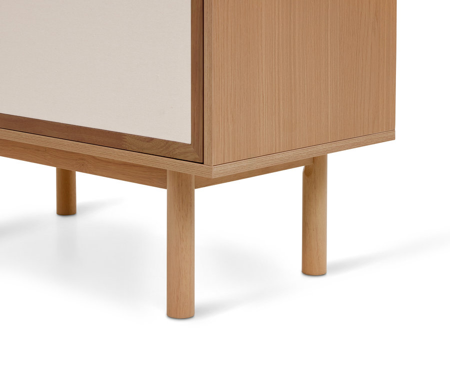Coin inférieur droit d'une armoire en bois clair avec quatre pieds ronds en bois et un panneau de porte beige clair.