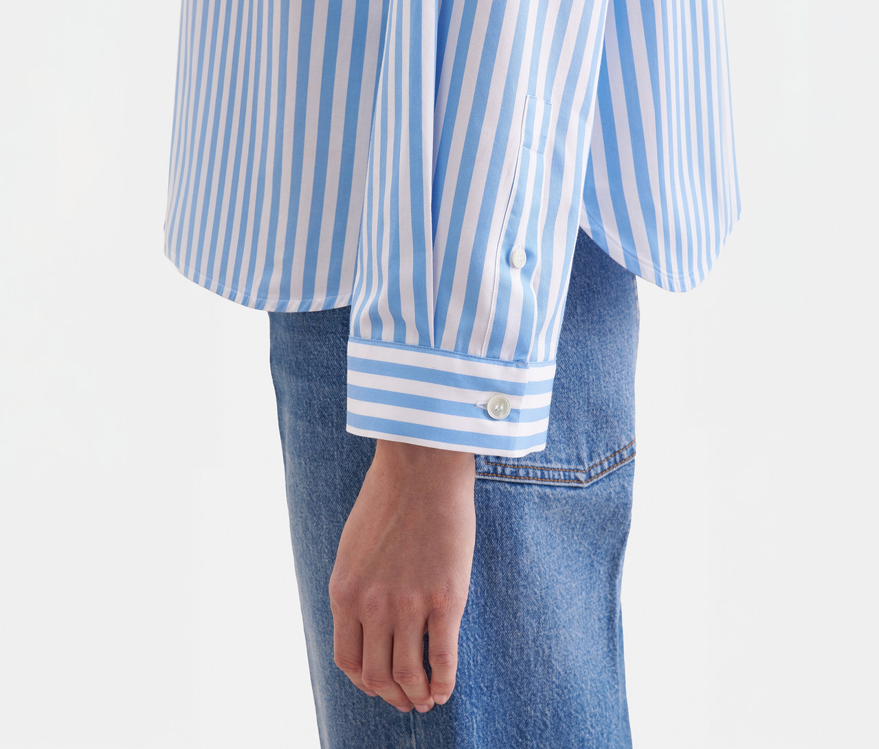 Gros plan d'une personne portant un chemisier oversize Seidensticker rayé bleu et blanc avec des poignets boutonnés, associé à un jean bleu.