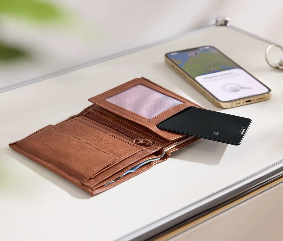 Un portefeuille marron ouvert, une carte noire, un téléphone portable doré et des clés sur une surface blanche.