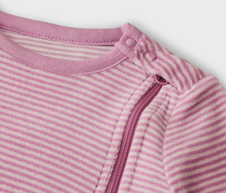 Gros plan d'un haut rayé rose avec un col rond, deux boutons-pression sur l'épaule gauche et une fermeture éclair diagonale sur l'épaule droite.