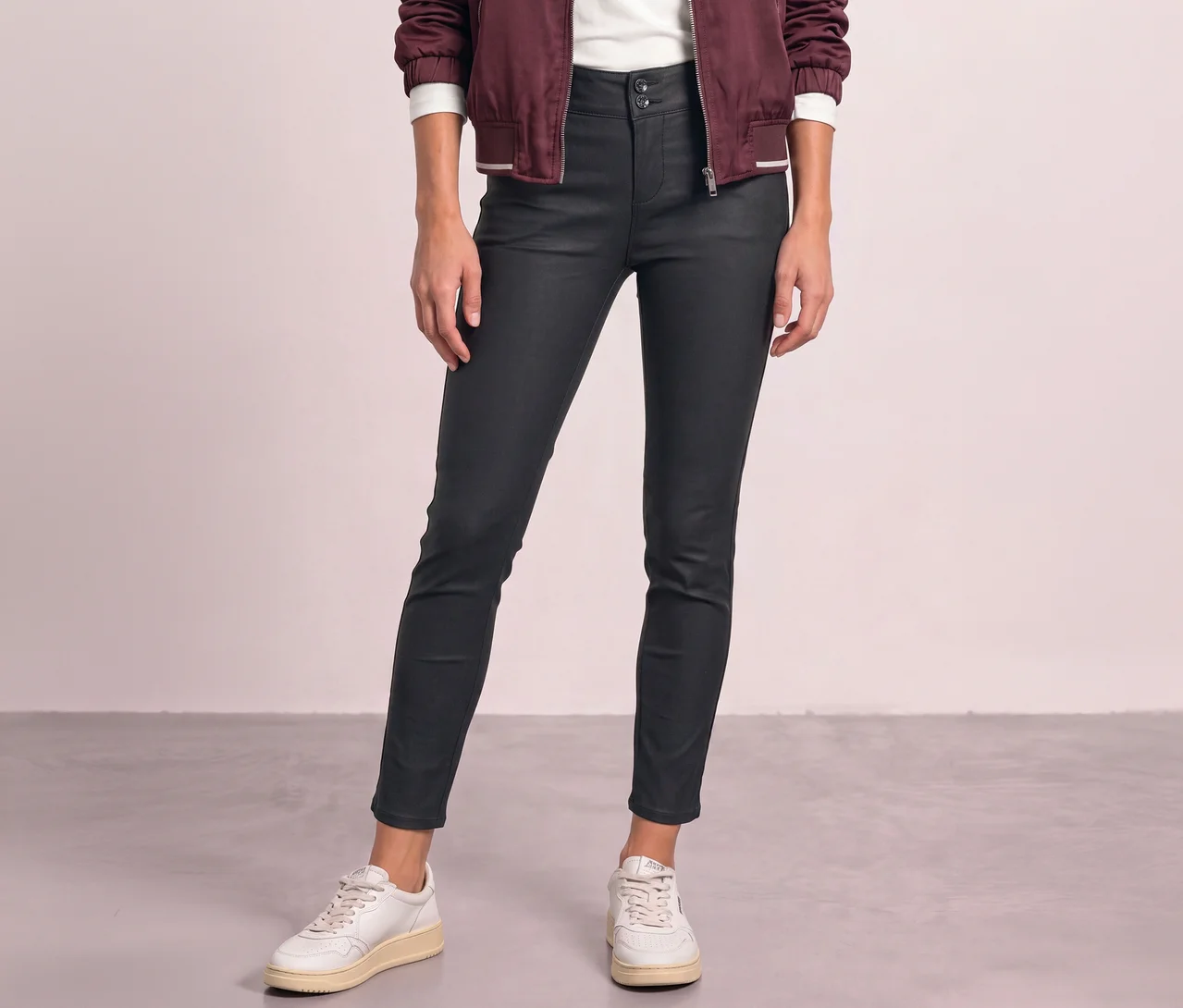 Une personne porte un pantalon Street One aspect cuir noir, un haut blanc, une veste bordeaux et des baskets blanches.