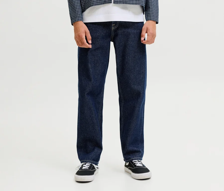 Une personne porte un jean Jack&Jones JJOriginal Chris bleu foncé, un t-shirt blanc, une veste à carreaux bleu et blanc et des baskets noires.
