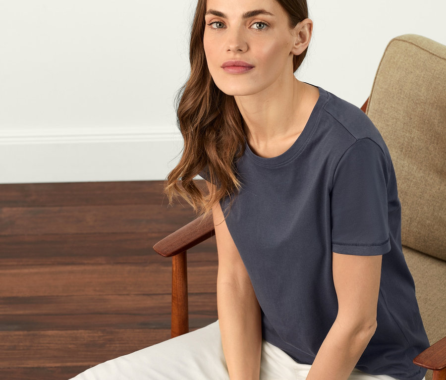 Une femme assise dans un fauteuil porte un t-shirt basique bleu acier.