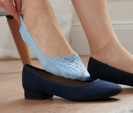 Une femme enfile une socquette bleu clair pour ballerines avec de la dentelle sur son pied chaussé d'une ballerine bleue.