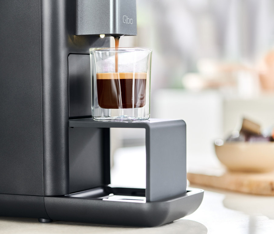 Le café est versé dans un verre à partir d'une machine à café Qbo ESSENTIAL Dark Stone.