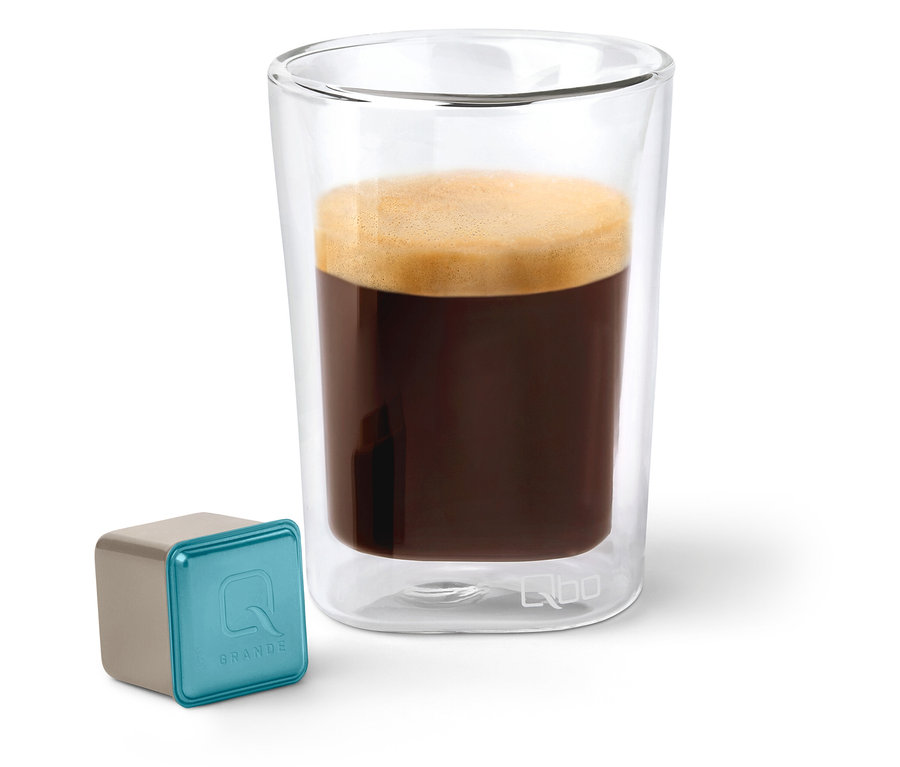 Capsule de café Qbo Caffè Grande KIRINYAGA BAYA à côté d'un verre de café.