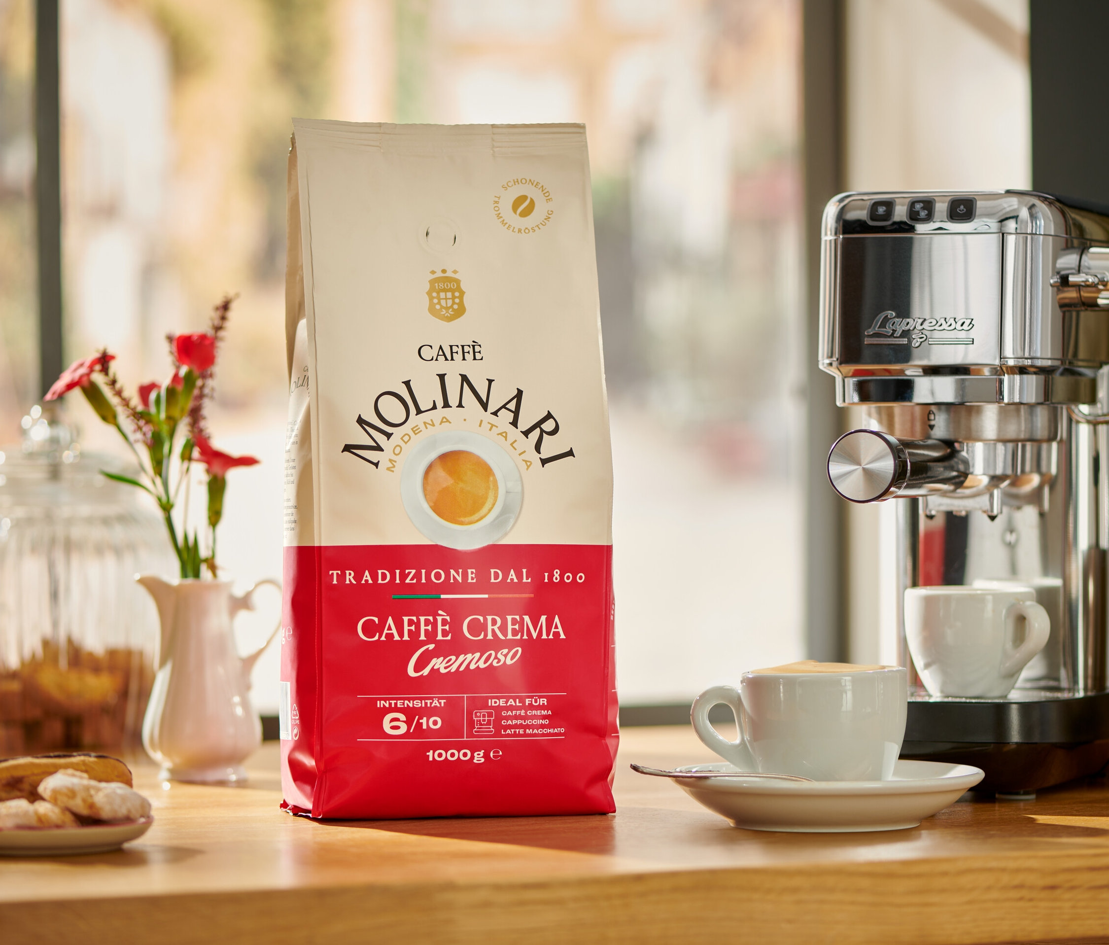 Un paquet de Caffè Molinari Caffè Crema Cremoso à côté d'une machine à café et d'une tasse de café.