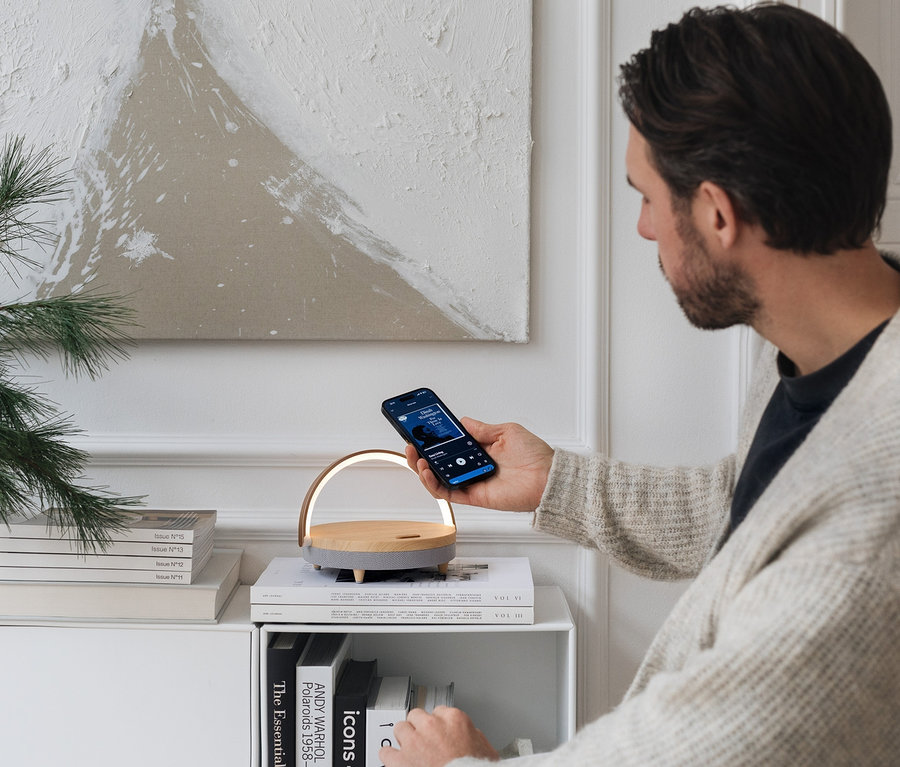 Un homme tient un téléphone au-dessus d'une enceinte Bluetooth® avec chargeur sans fil et veilleuse LED.