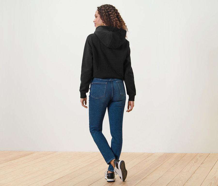 Femme vue de dos portant un jean skinny Fit « Hanna » bleu et un sweat à capuche noir.