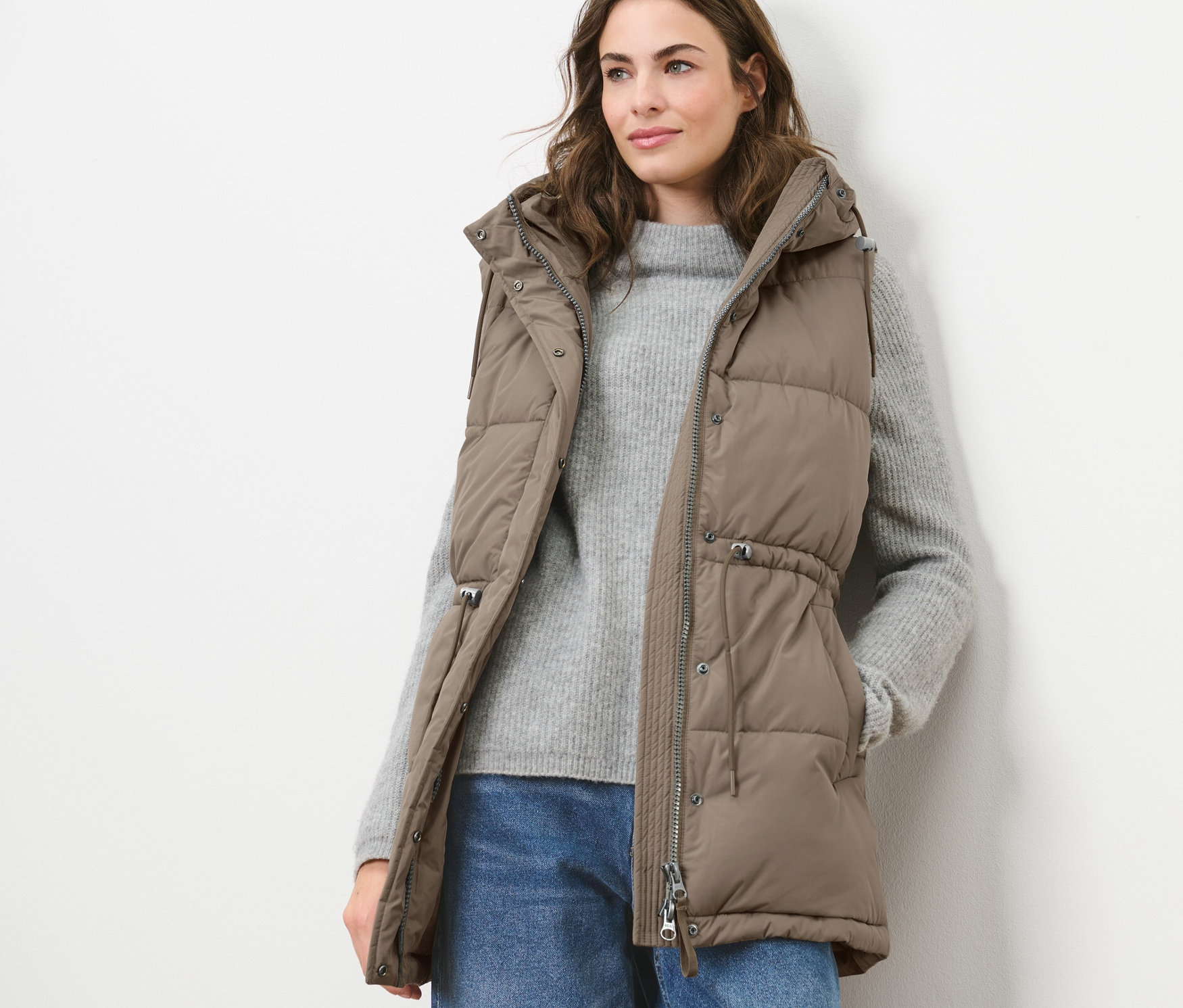 Une femme portant un gilet sans manches matelassé à capuche, un pull et un jean.