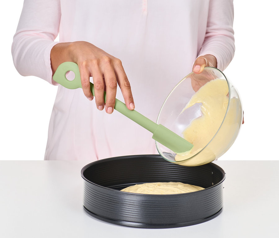 Une femme verse de la pâte d'un bol dans un moule à gâteau avec une cuillère multifonction.