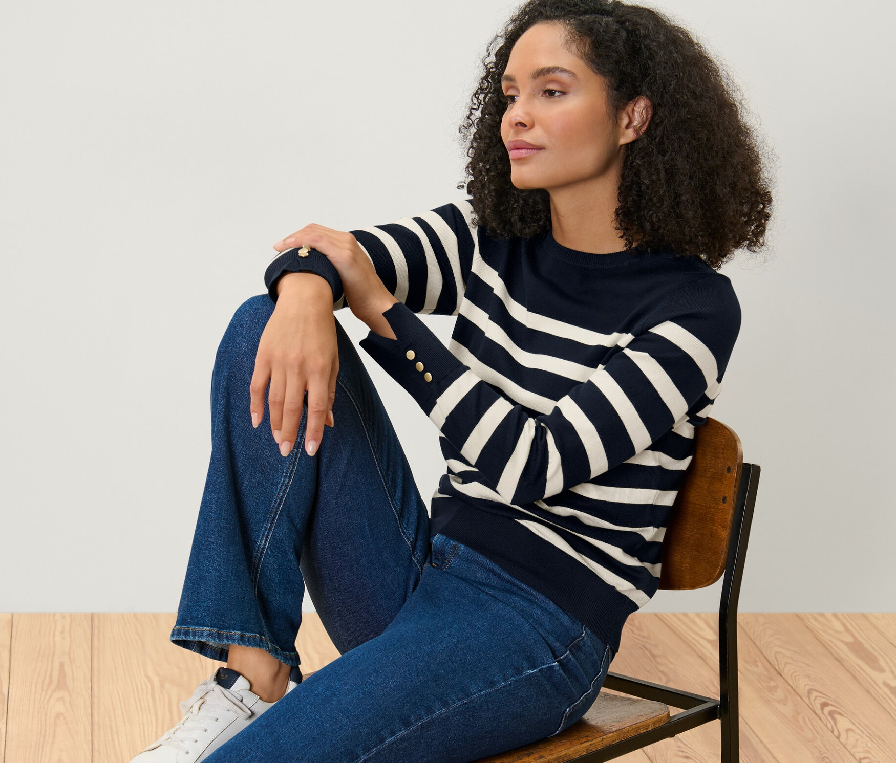Femme assise sur une chaise portant un pull en maille fine rayé bleu foncé.
