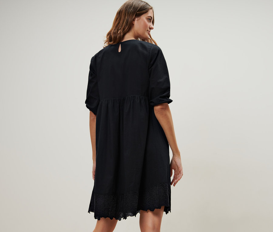 Femme debout, vue de dos, portant une robe tissée noire avec broderie.