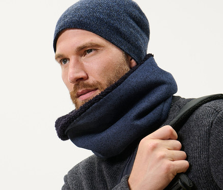 Un homme barbu portant une écharpe-tube et un bonnet en polaire tricotée bleu foncé et portant un sac à dos.