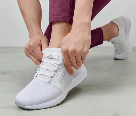 Femme nouant des lacets élastiques sur une chaussure blanche.