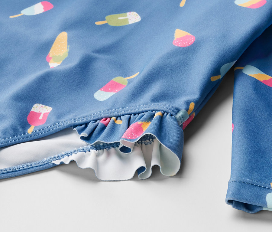Gros plan sur un maillot de bain bleu pour enfant avec des motifs de glaces et un indice de protection UV 80.