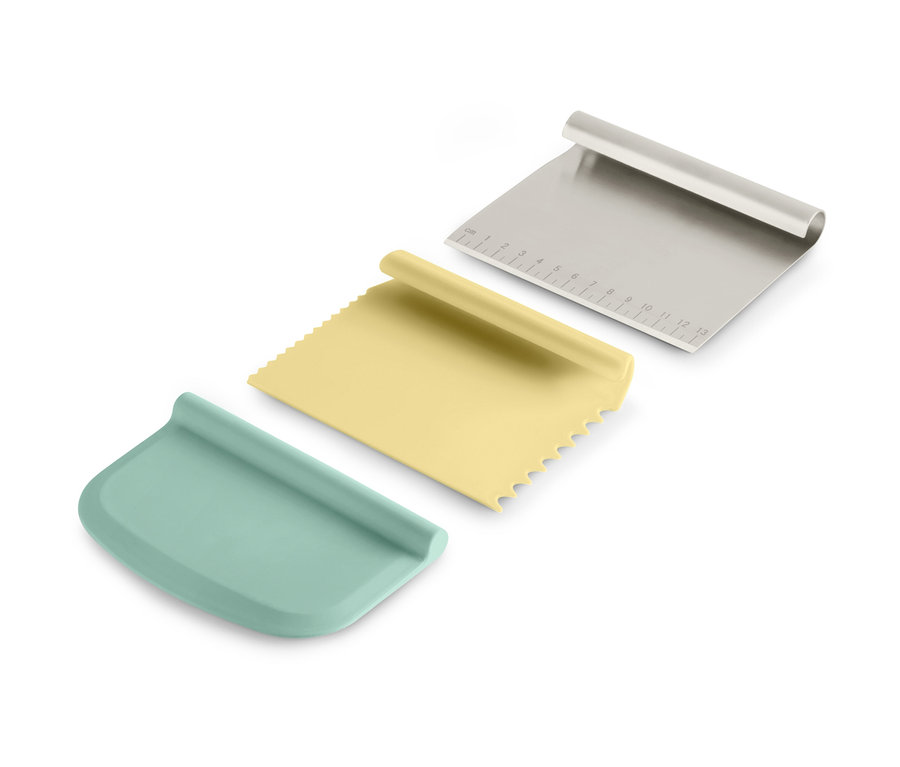 Trois grattoirs du kit d'accessoires professionnels de pâtisserie, un argenté, un jaune et un bleu-vert.