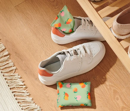 Deux coussins rafraîchissants à motif de pêche sont posés à côté de chaussures blanches sur un plancher en bois.