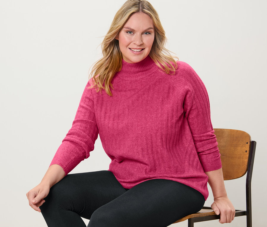 Une femme est assise sur une chaise et porte un pull en maille côtelée à col montant et un legging thermique.