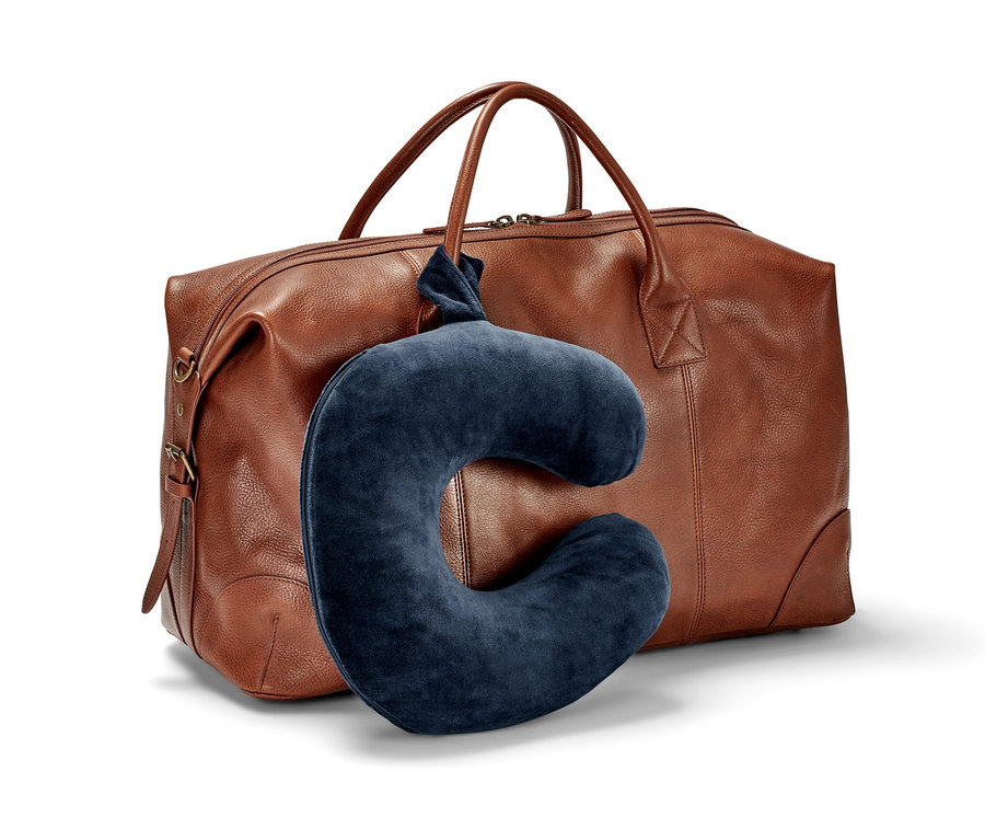 Un coussin de nuque bleu marine en mousse à mémoire de forme appuyé contre un sac de voyage en cuir marron.