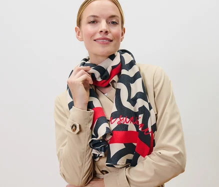Femme posant en trench-coat beige avec une écharpe tissée imprimée.