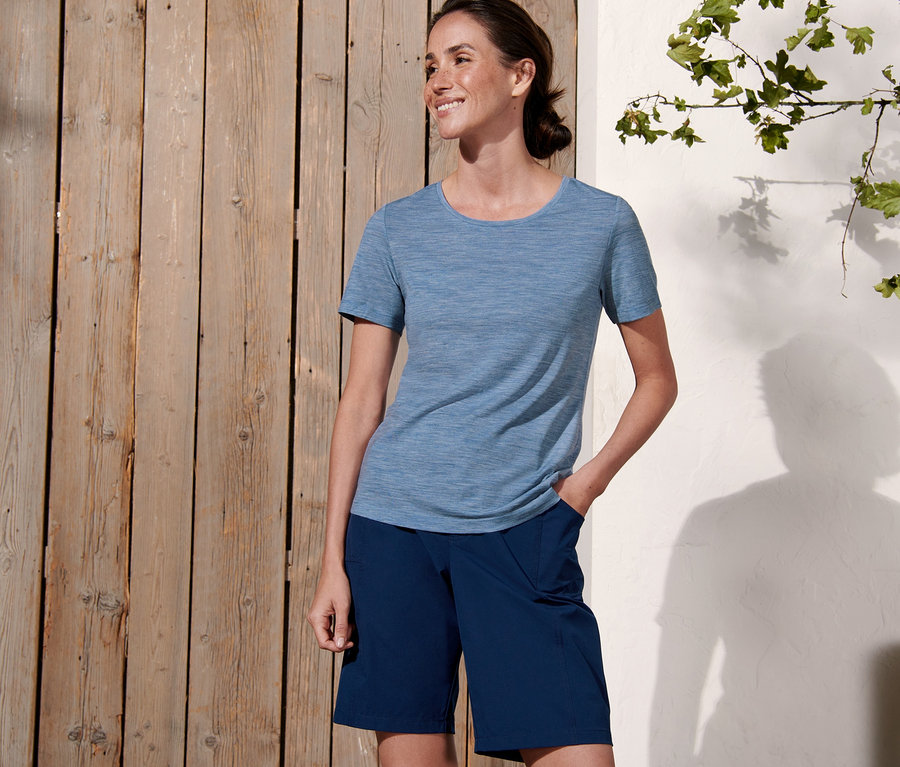 Une femme pose à l'extérieur et porte un t-shirt fonctionnel bleu foncé en laine mérinos et un short bleu foncé.