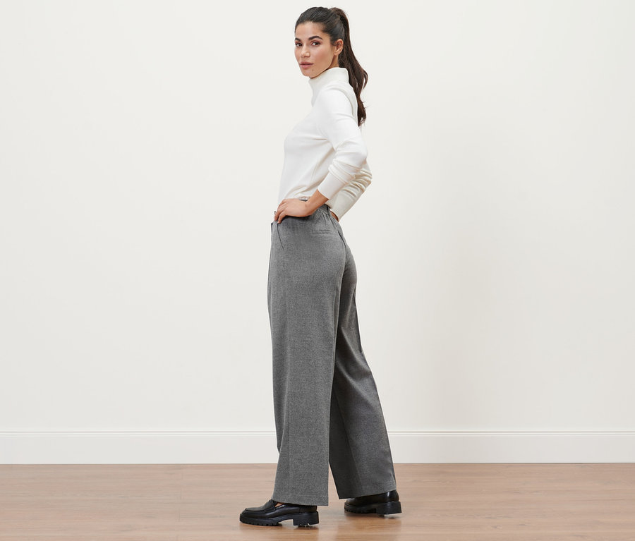 Femme posant en pantalon tissé gris et col roulé blanc.