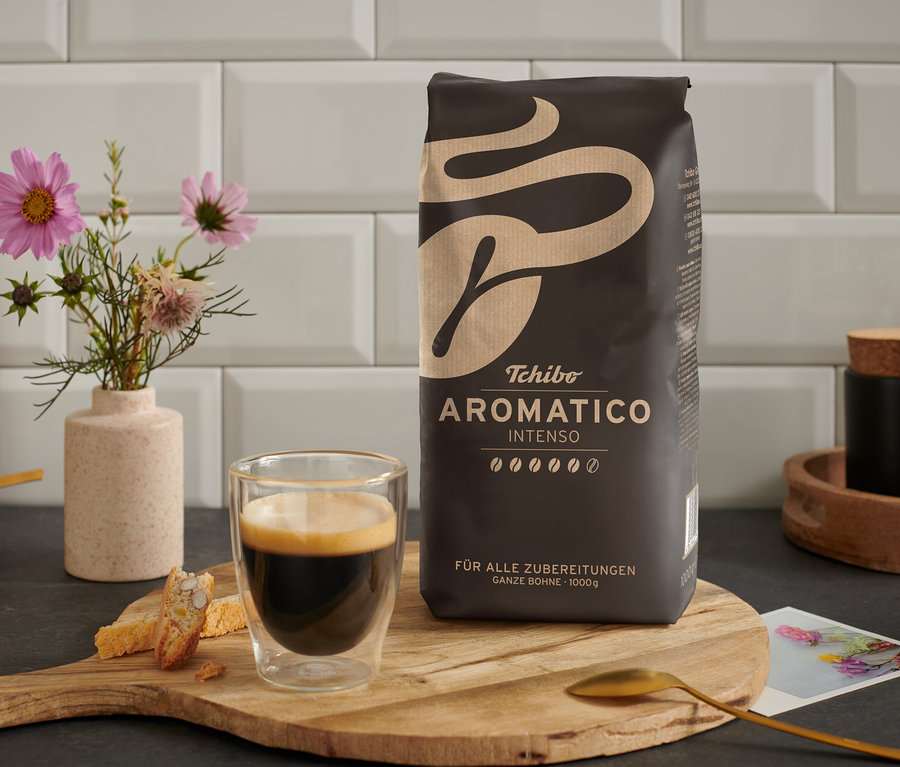 Une tasse de café est posée à côté d'un paquet de café en grains Aromatico Intenso - 1 kg sur une table en bois.