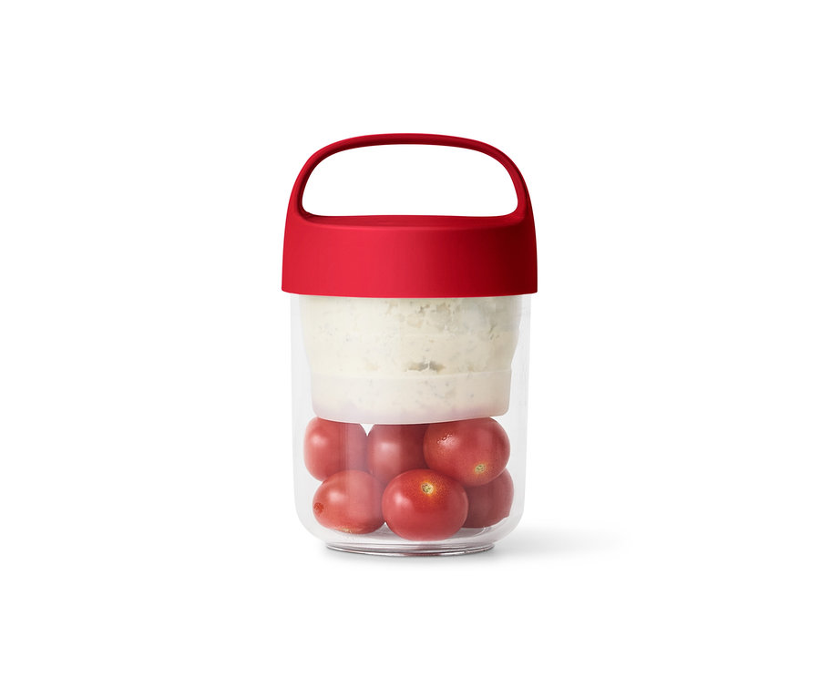 Un récipient transparent avec un couvercle rouge contient des tomates et de la salade.