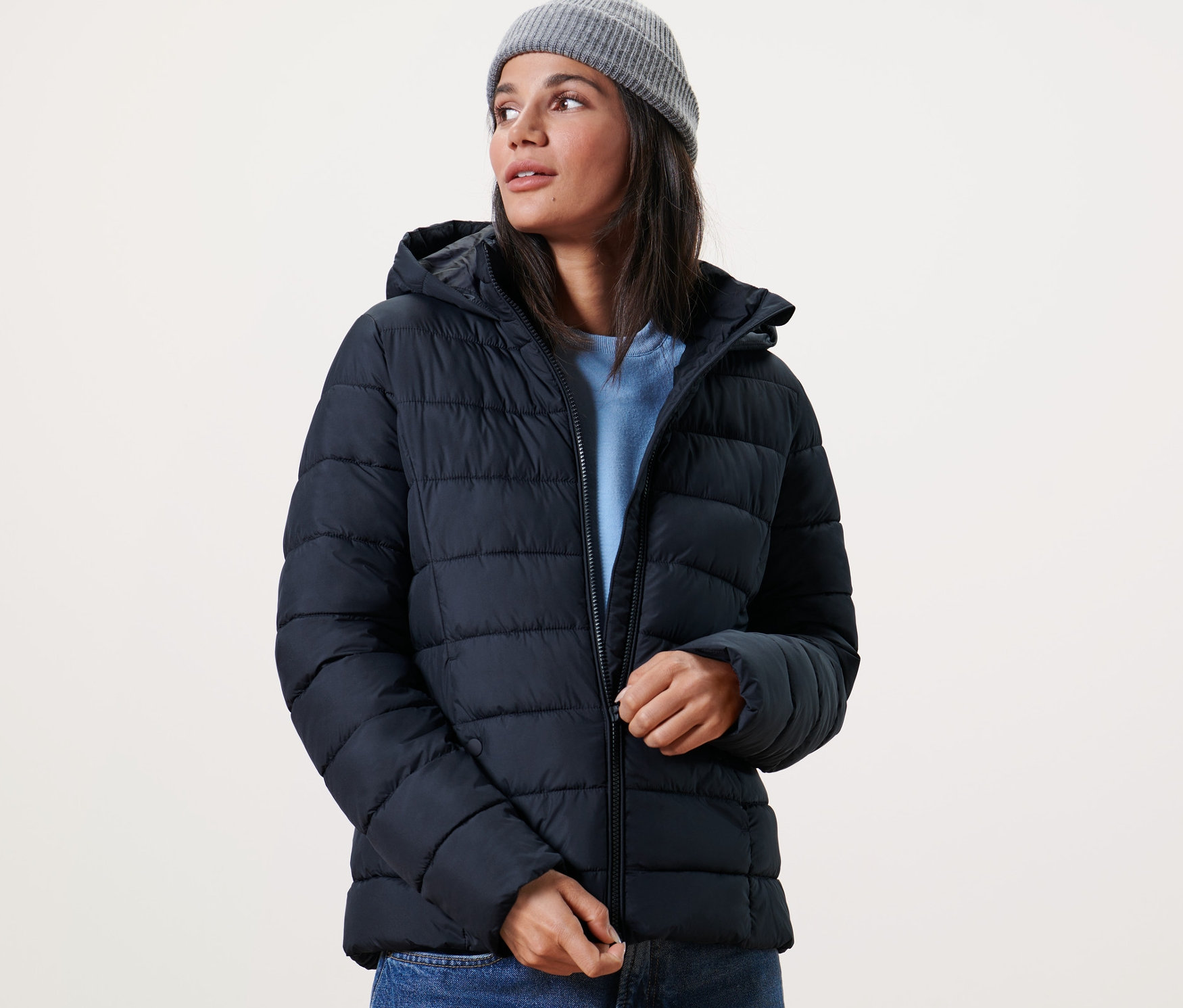 Femme fermant une veste matelassée à capuche bleu foncé et portant un bonnet gris.