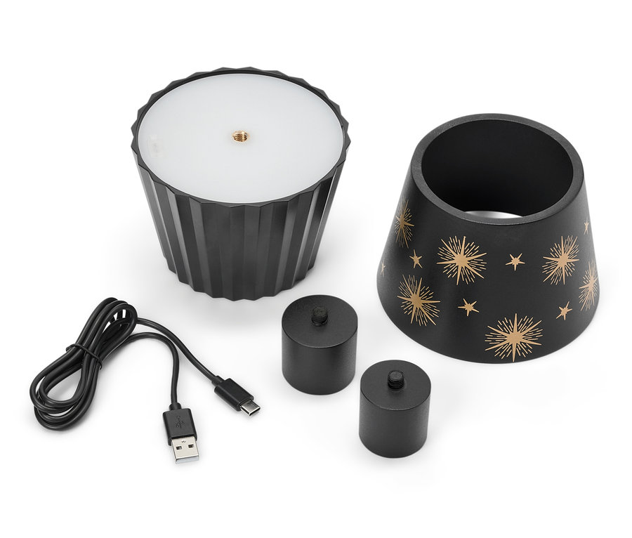 Une lampe noire avec des étoiles, deux bougies noires et un câble USB sont posés sur un fond blanc.