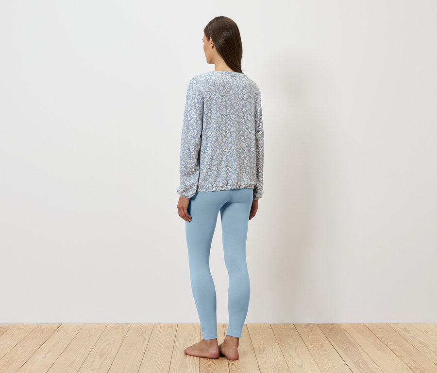 Une femme, vue de dos, porte un legging bleu et un chemisier à motifs.