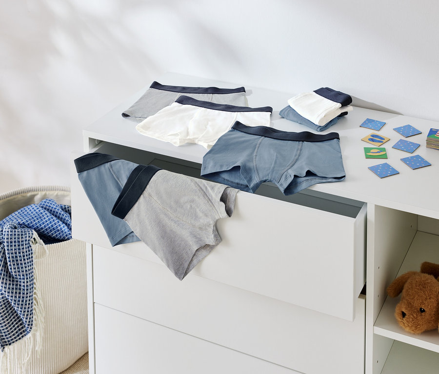 Vue de sous-vêtements pour enfants sur une commode et dans un tiroir ouvert, à côté d'un panier à linge et d'un animal en peluche.