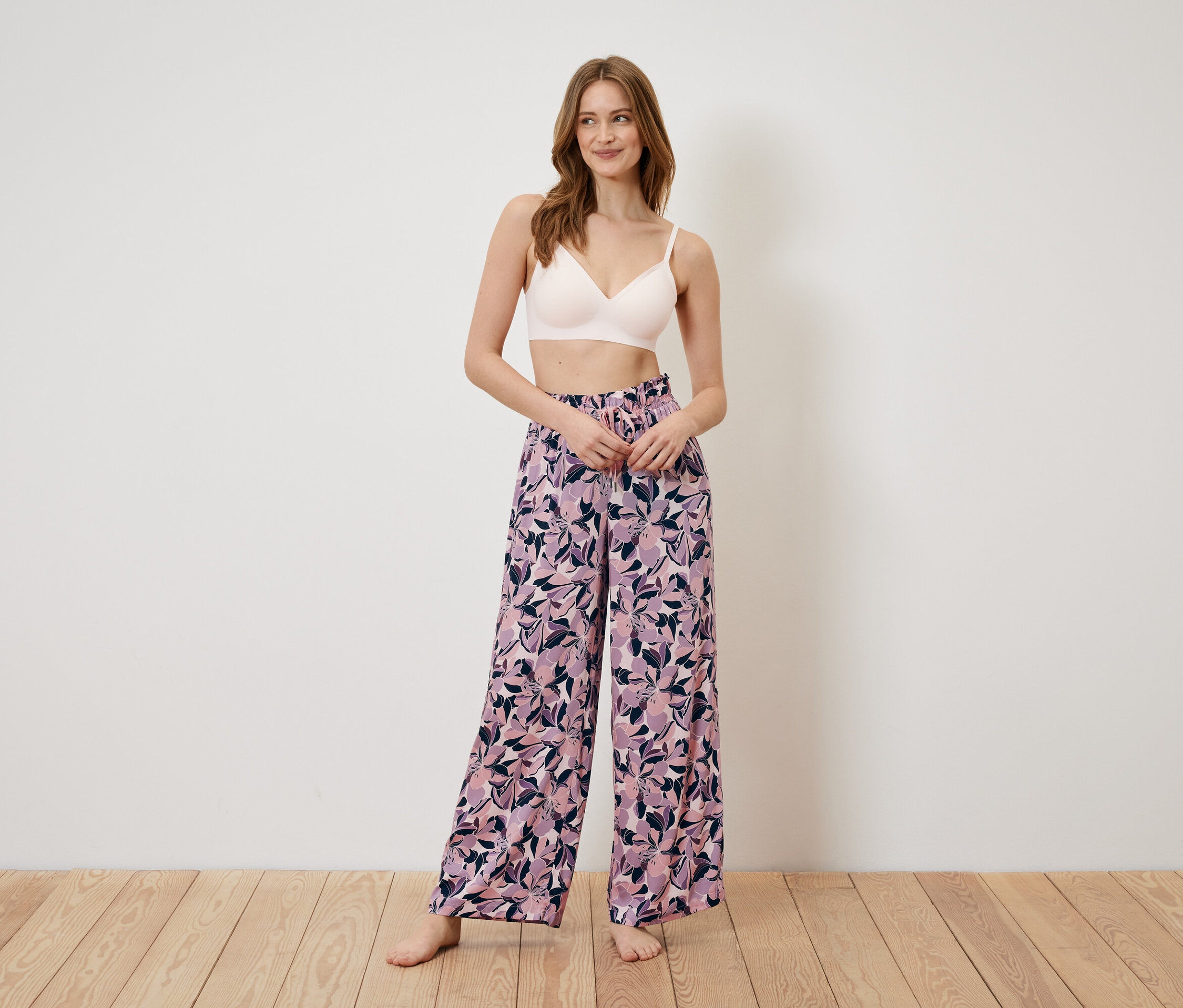 Une femme debout porte un soutien-gorge et un pantalon large à motifs floraux.