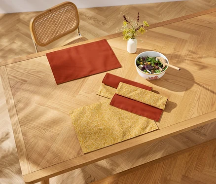 Vue de dessus d'une table en bois avec des sets de table, des serviettes et un saladier.