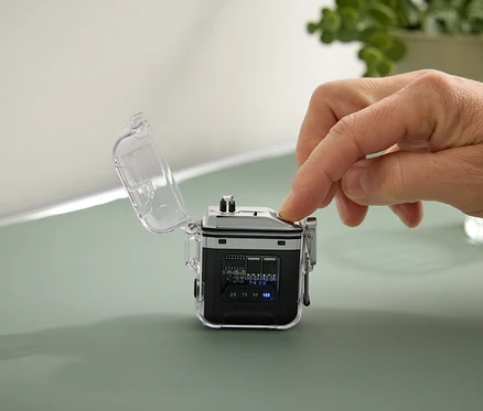 Une main appuie sur un bouton d'un petit appareil noir avec un boîtier transparent.