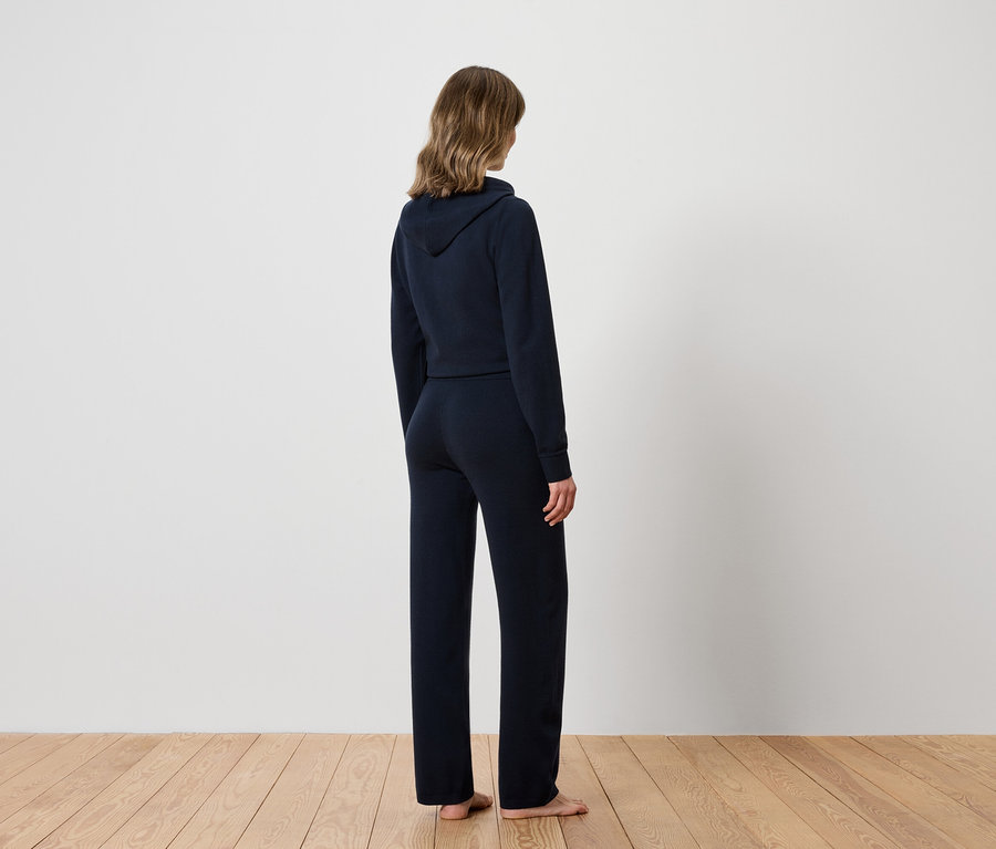 Une femme, dos à la caméra, porte un sweat à capuche bleu marine et un pantalon de survêtement.