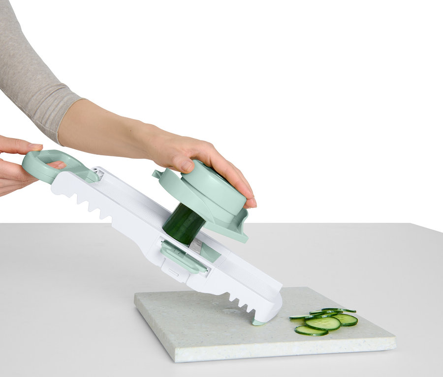 Une femme tranche un concombre avec une trancheuse à légumes dotée d'une poignée et d'un accessoire rotatif.