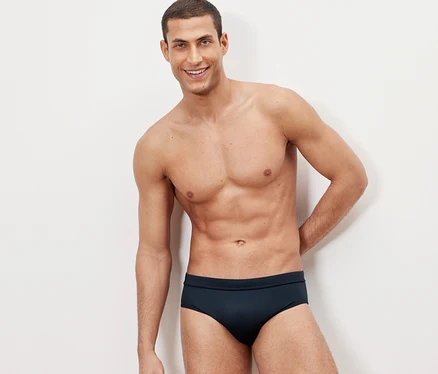 Un homme pose devant un fond blanc en slip de bain.