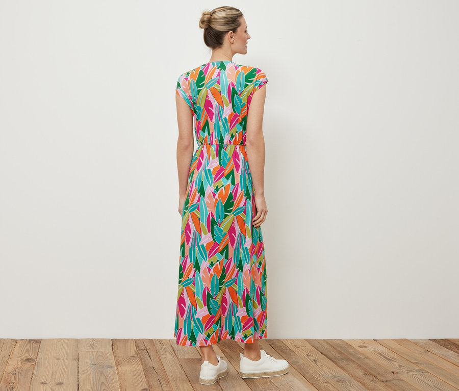 Une femme se tient dos à la caméra et porte une robe en jersey avec nœud et des baskets blanches.