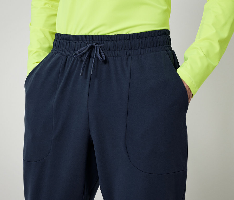 Personne en chemise vert néon et pantalon bleu marine avec les mains dans les poches.