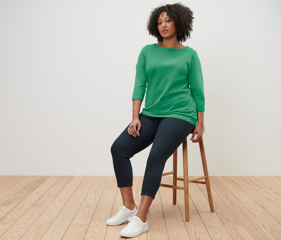 Femme assise sur un tabouret portant un t-shirt vert à manches 3/4.