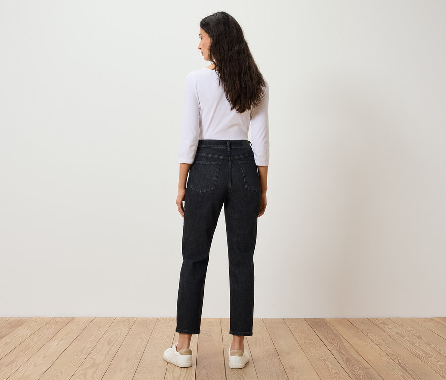 Une femme, vue de dos, porte un t-shirt blanc à manches trois-quarts et un jean noir.