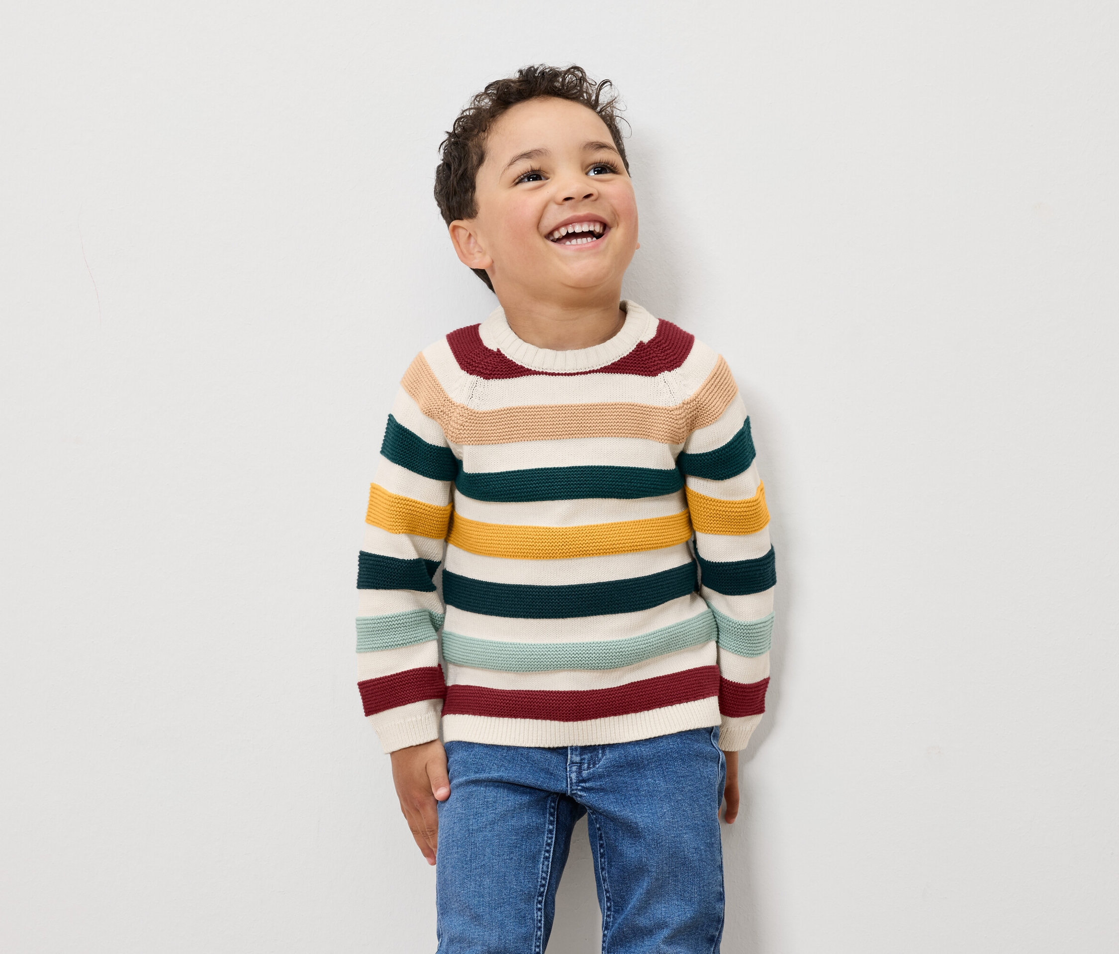 Un garçon rit et porte un pull rayé et un jean.