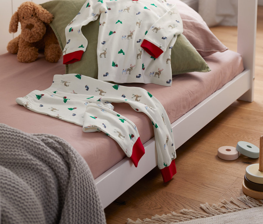 Un pyjama en interlock de coton bio et un chien en peluche sont posés sur un lit.