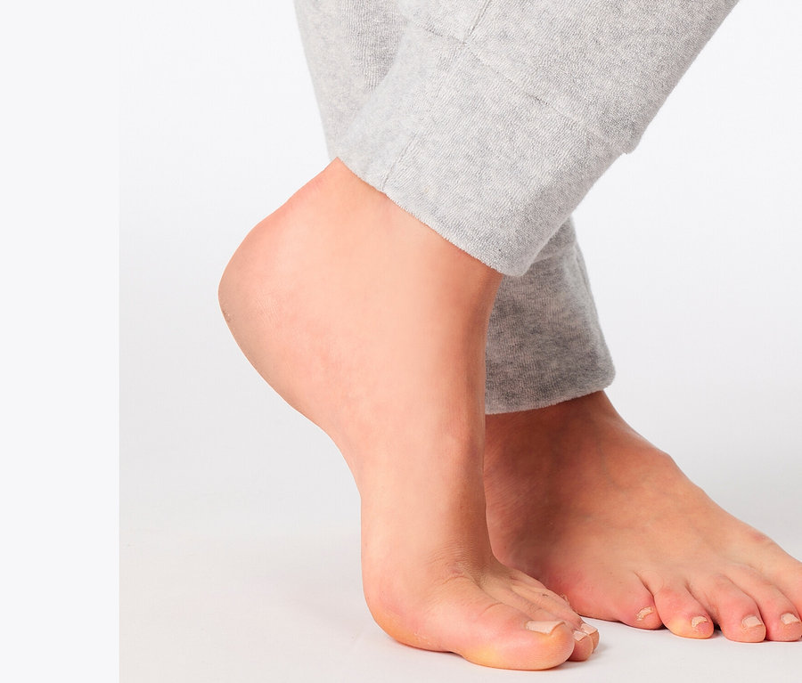 Pieds d'une personne se tenant sur un fond blanc et portant un pantalon de survêtement gris.