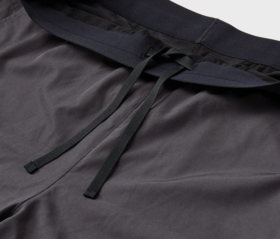 Détail d'un pantalon de survêtement gris avec une taille élastique noire et des cordons de serrage.