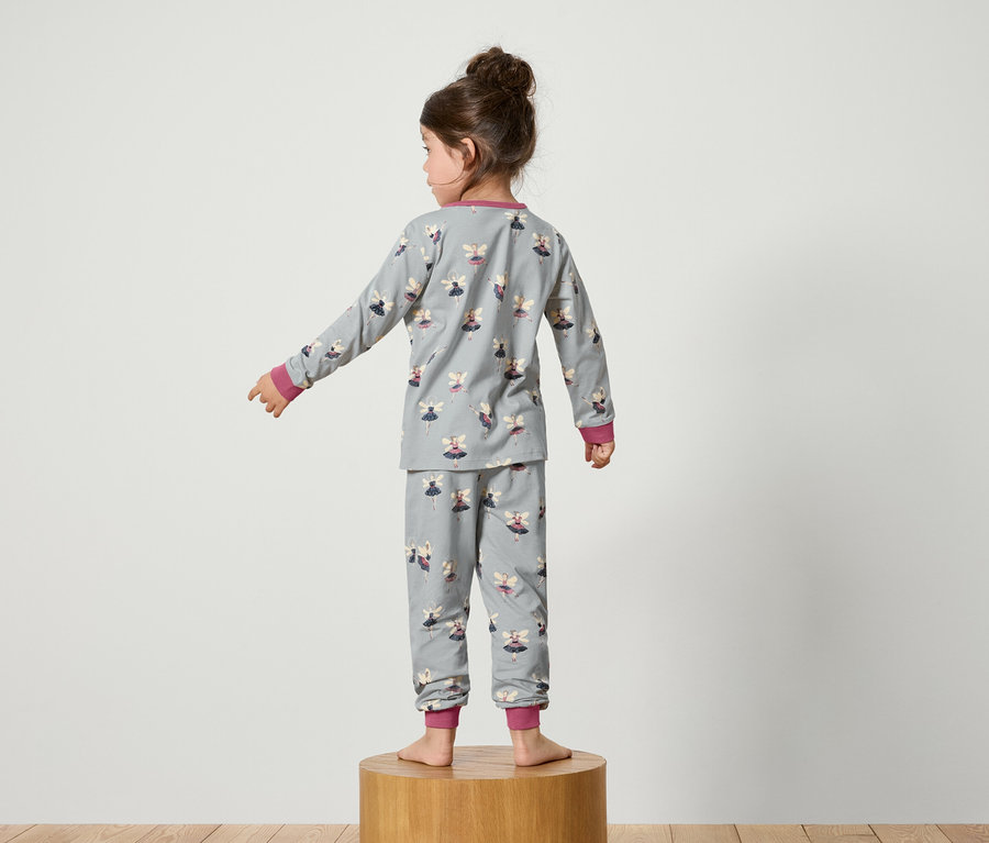 Une fille se tient dos à la caméra, portant un pyjama gris imprimé avec des fées.