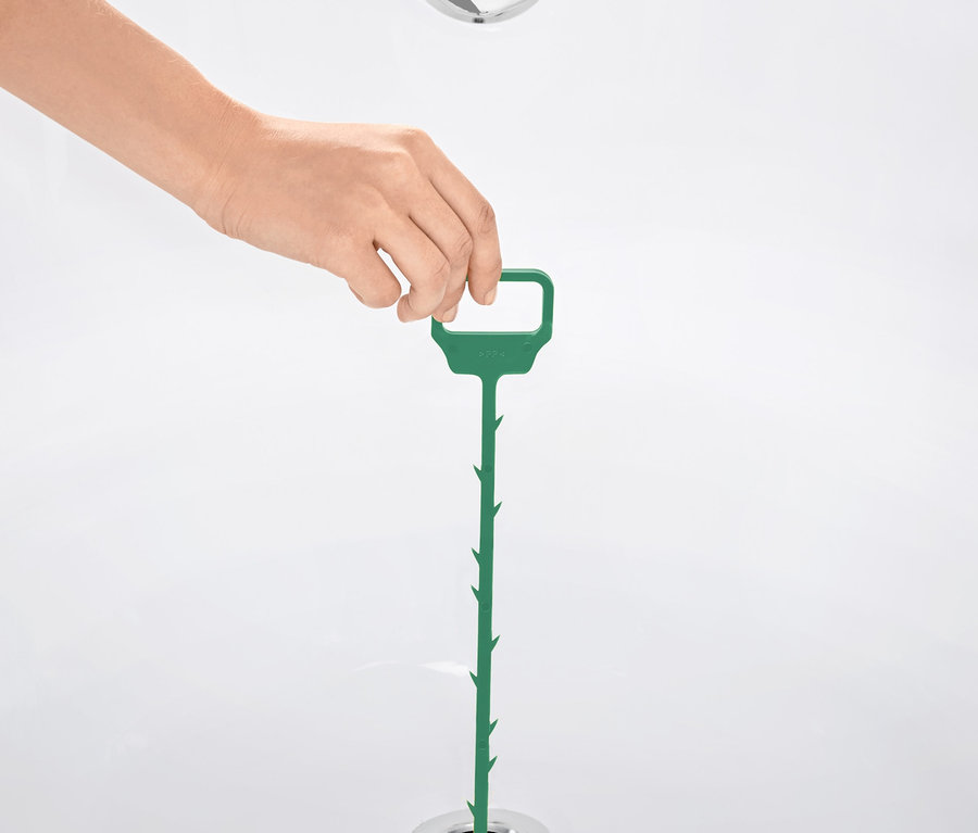 Une main insère une tige de curage verte dans le drain d'une baignoire.