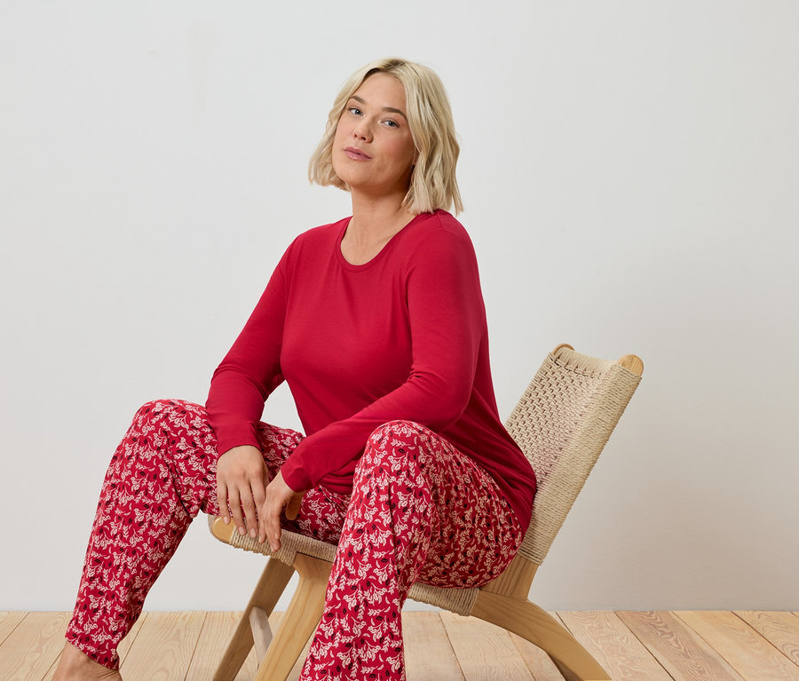 Une femme blonde est assise sur une chaise en osier et porte un pyjama rouge.